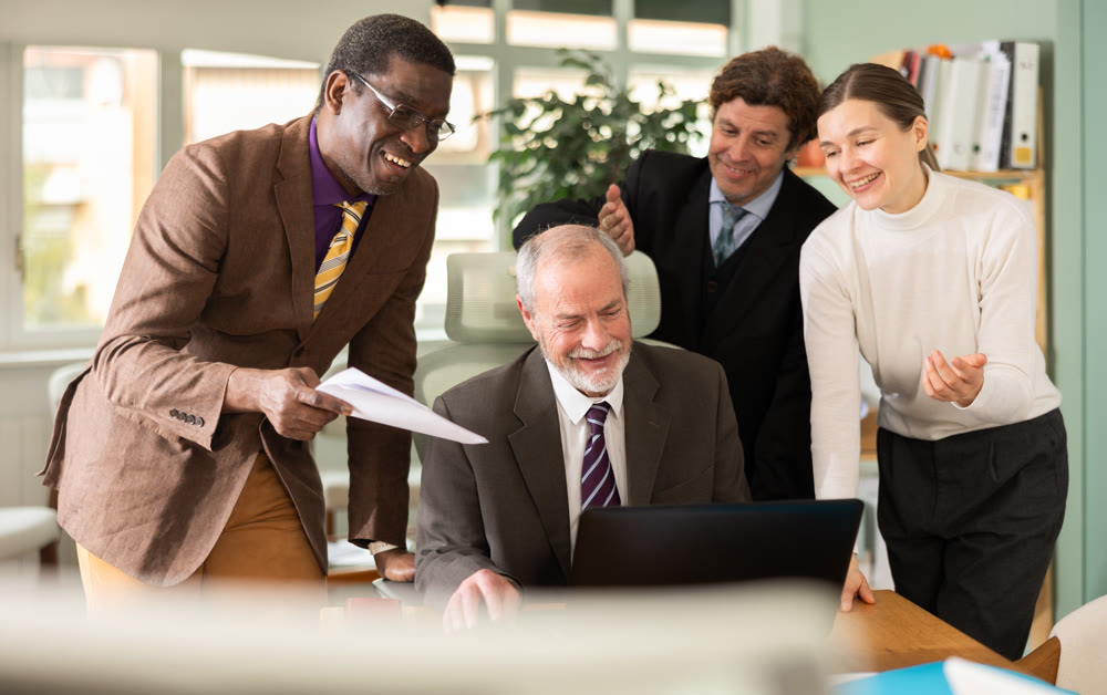 Team of businessmen laugh at funny video posted online during coffee break