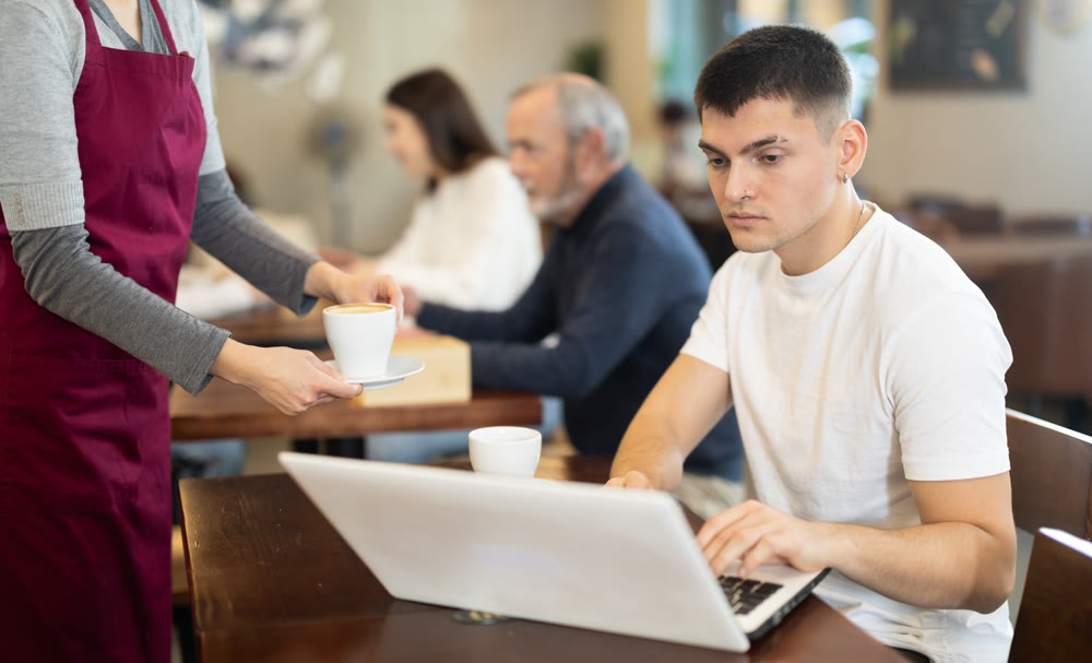 Guy works on laptop and drinks coffee in cafe interior