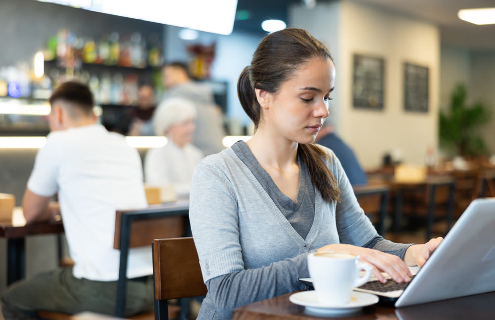 Girl works on a laptop and drinks coffee in cafe interior