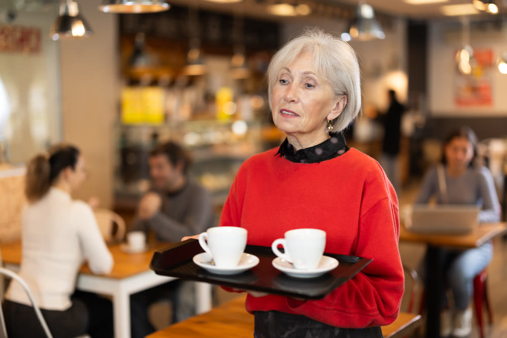Breakfast in cafe - mature woman carries tray with two cups of coffee