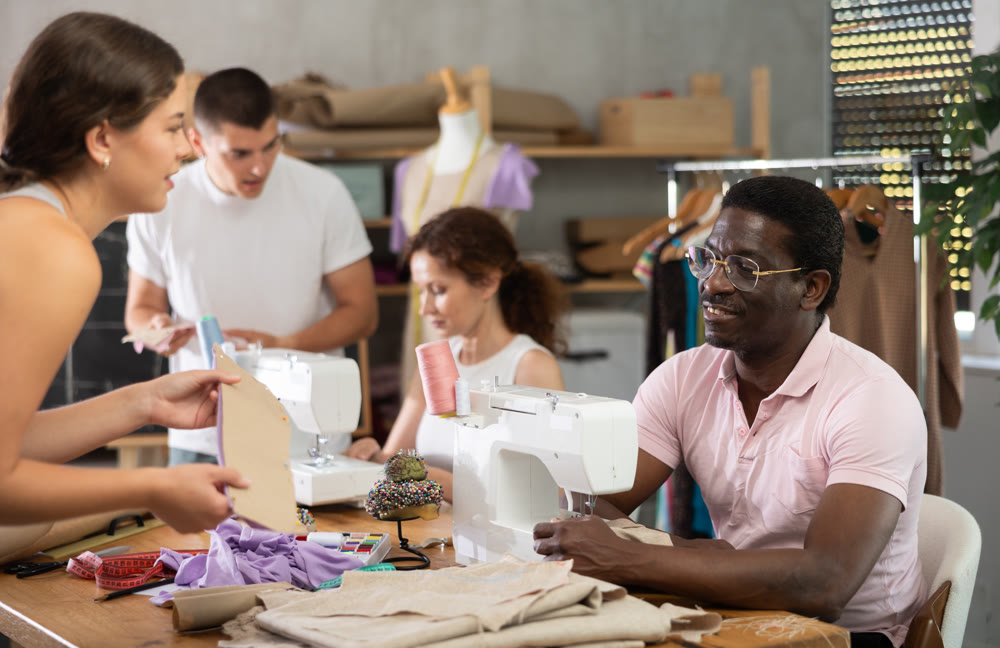 Male sewing course student working and exchanging ideas with classmate