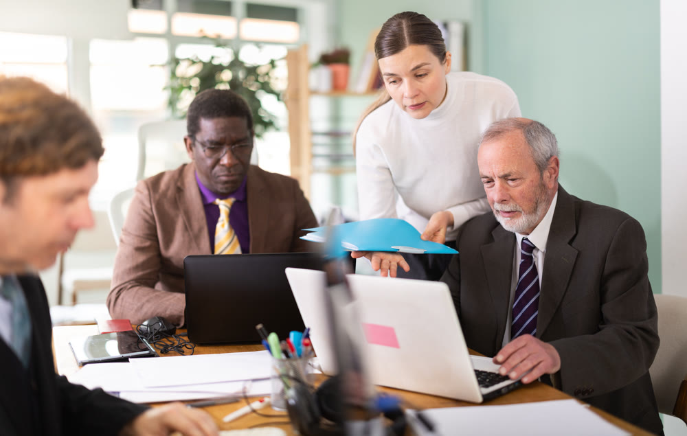 Experienced employee helping elderly worker with laptop