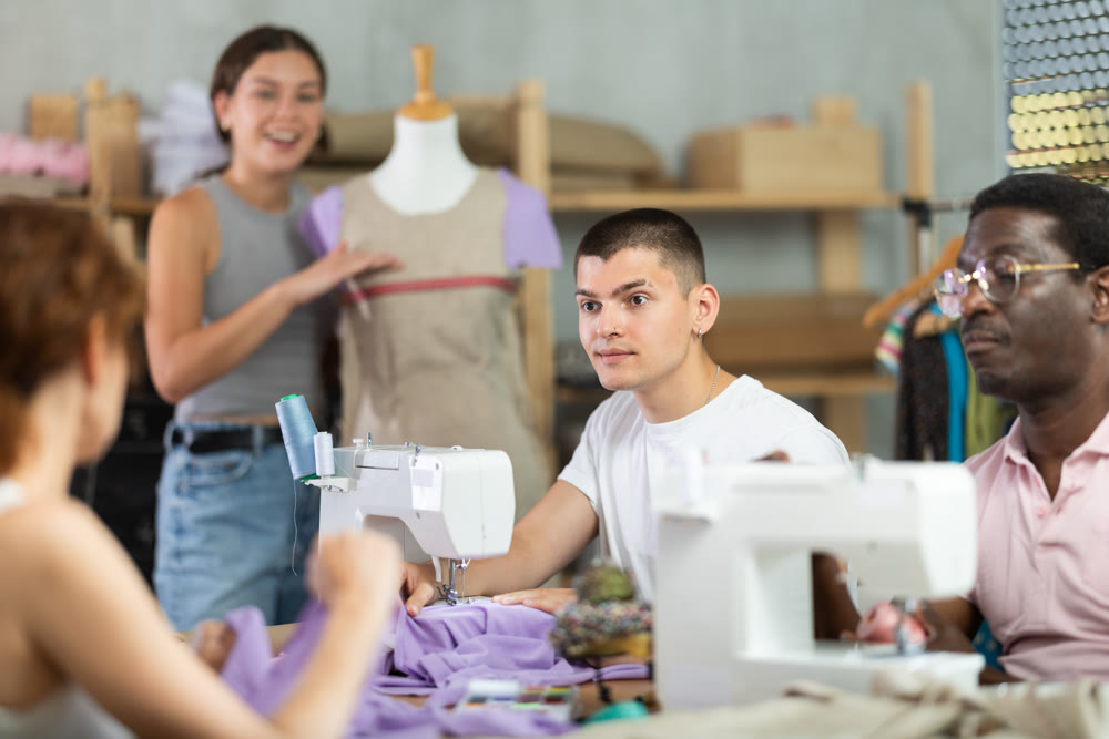 Young guy talking with woman and sewing, other working with mannequin