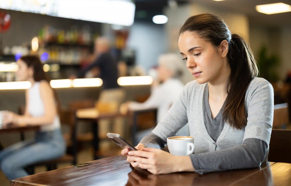 Girl in cafe drinks coffee and using mobile phone