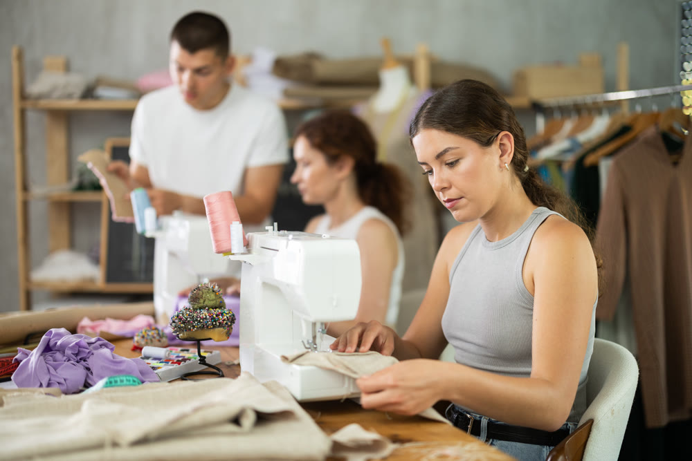 Engaged girl stitching fabric on machine in sewing class for adults