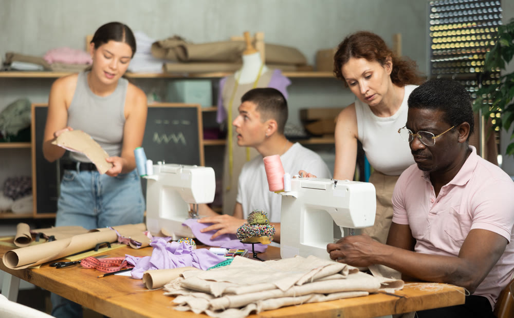 Middle-aged female teacher helping students sew while other works with textile