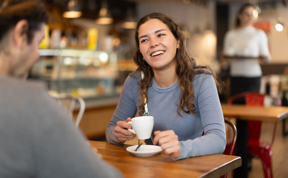 Girl in cafe sits opposite male companion, has nice conversation
