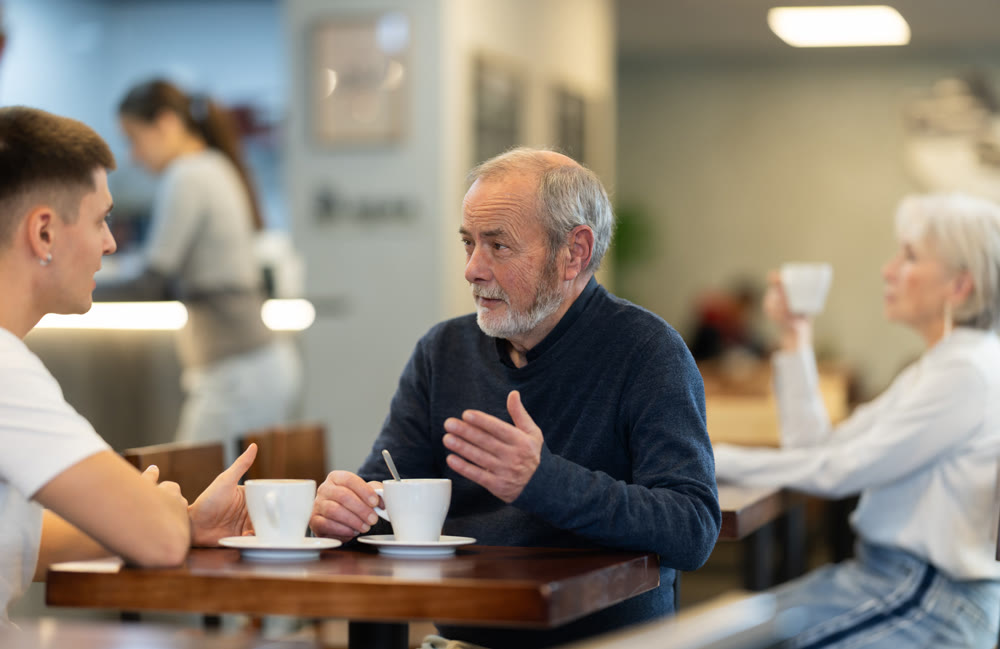 Mature man and her adult son sit together at table in cafe