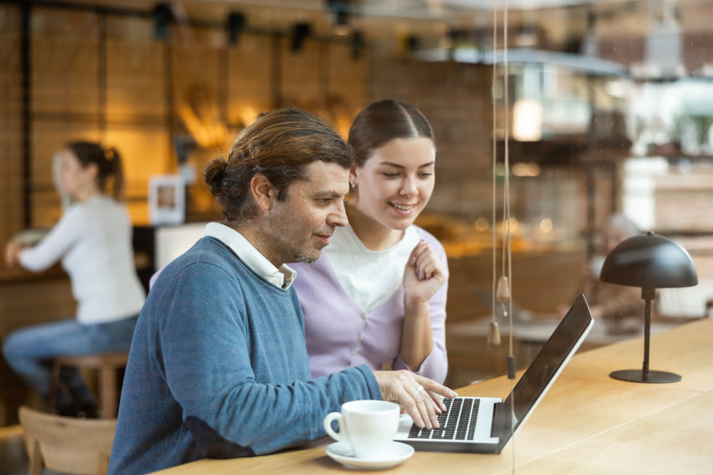 Man and woman looking at laptop screen while having lunch at bar counter of cafe