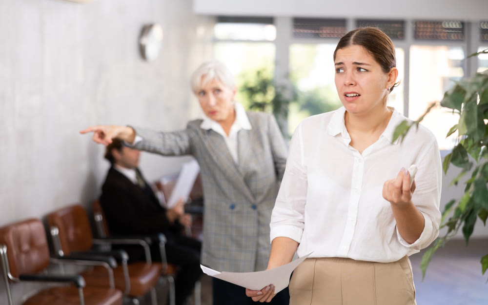 Crying young female office worker scolded by angry woman boss