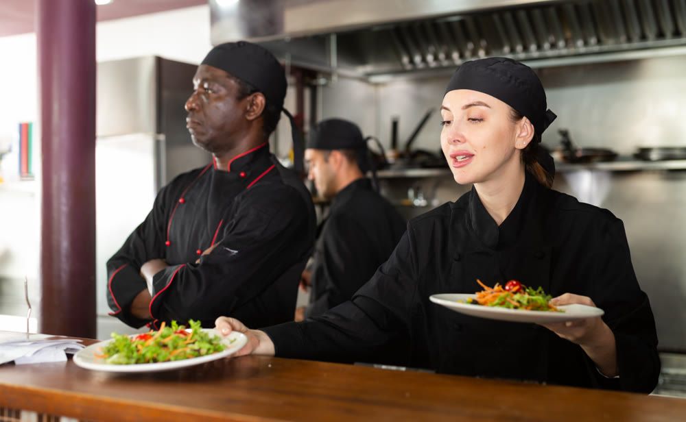 Female chef puts in black uniform ready meals on shelves in restaurant