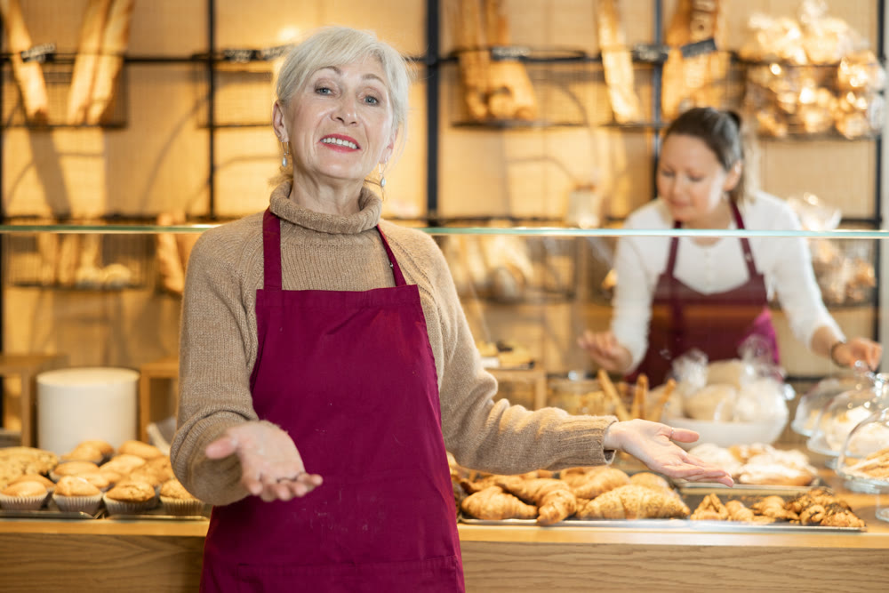 Cheerful mature female baker welcoming everyone into her bakery