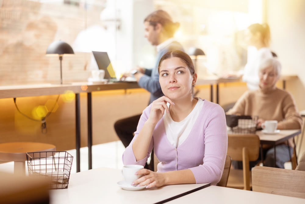 Dreamy young girl drinking coffee in cozy cafe