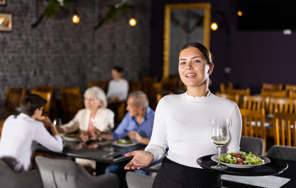 Young woman waiter posing with tray in restaurant
