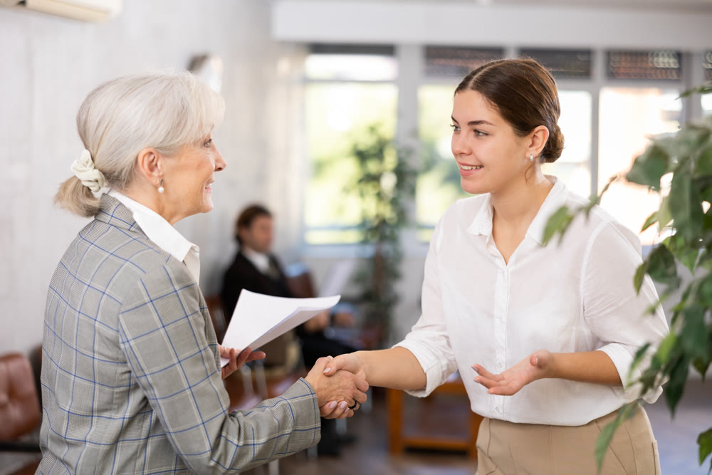 Positive young woman shaking hands with aged female business partner