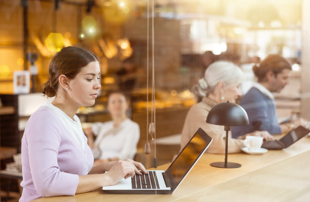 Young female freelancer sitting in cafe with cup of coffee and laptop