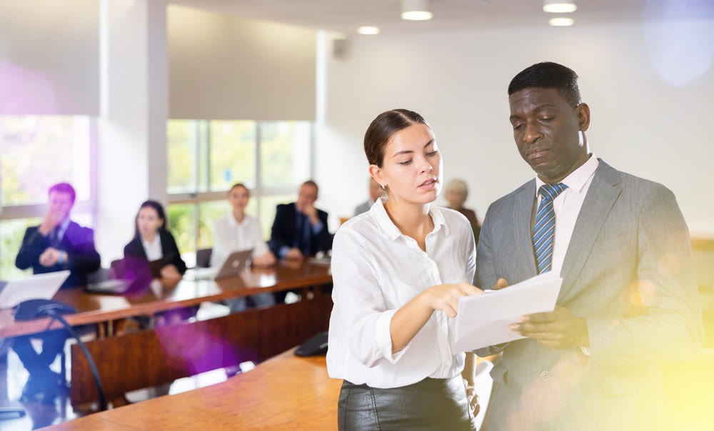 Secretary and employer discussing documentation during business meeting