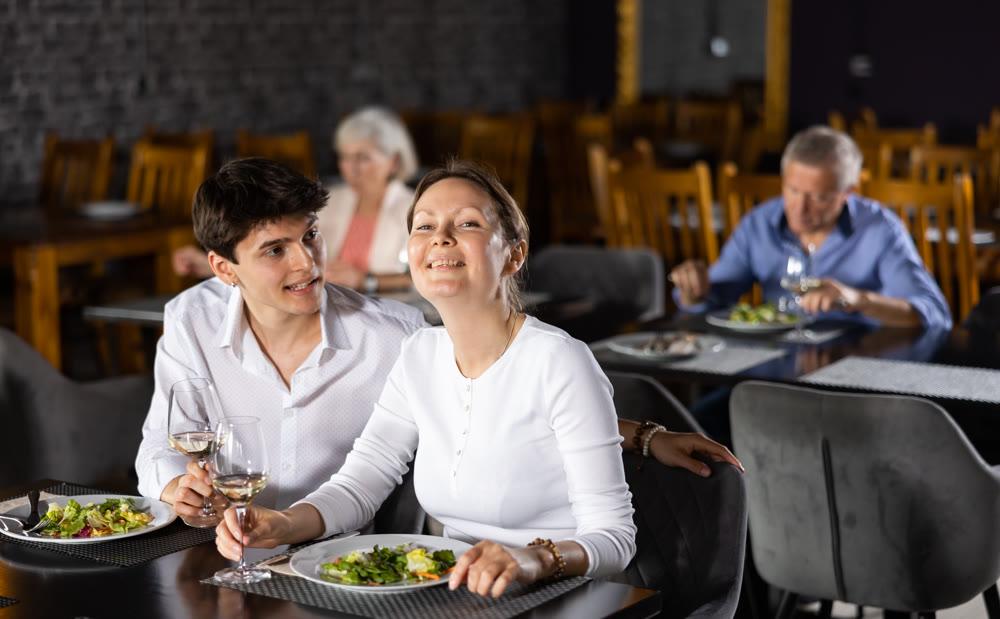 Young man and adult woman having dinner in restaurant