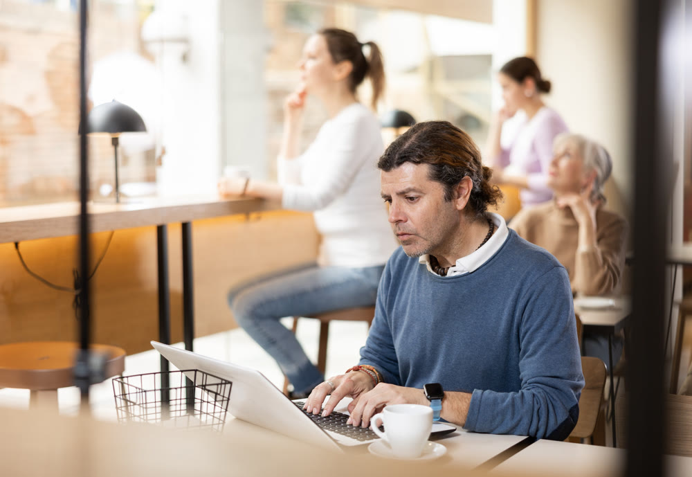 Focused man drinking coffee while working on laptop in cozy cafe