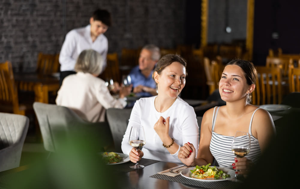 Young and adult women having dinner in restaurant