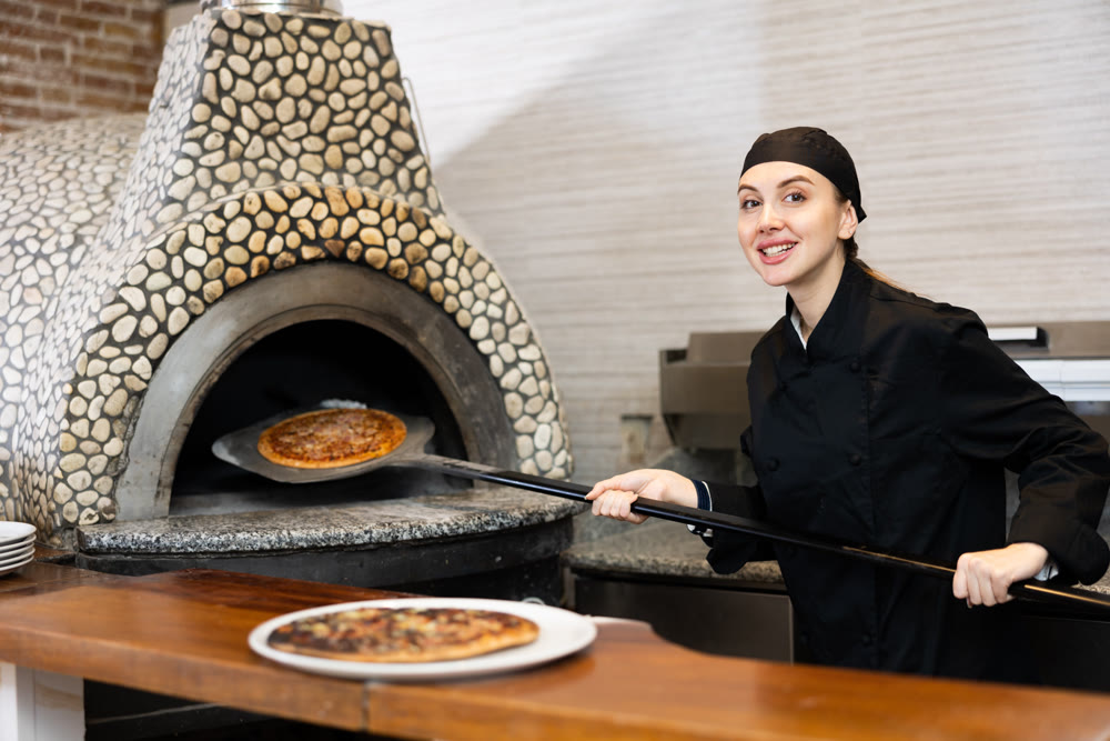 Smiling woman chef preparing pizza in restaurant