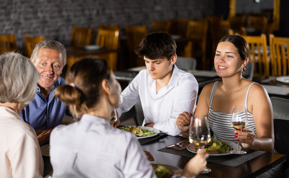 Elderly couple and young couple and adult woman having dinner in restaurant