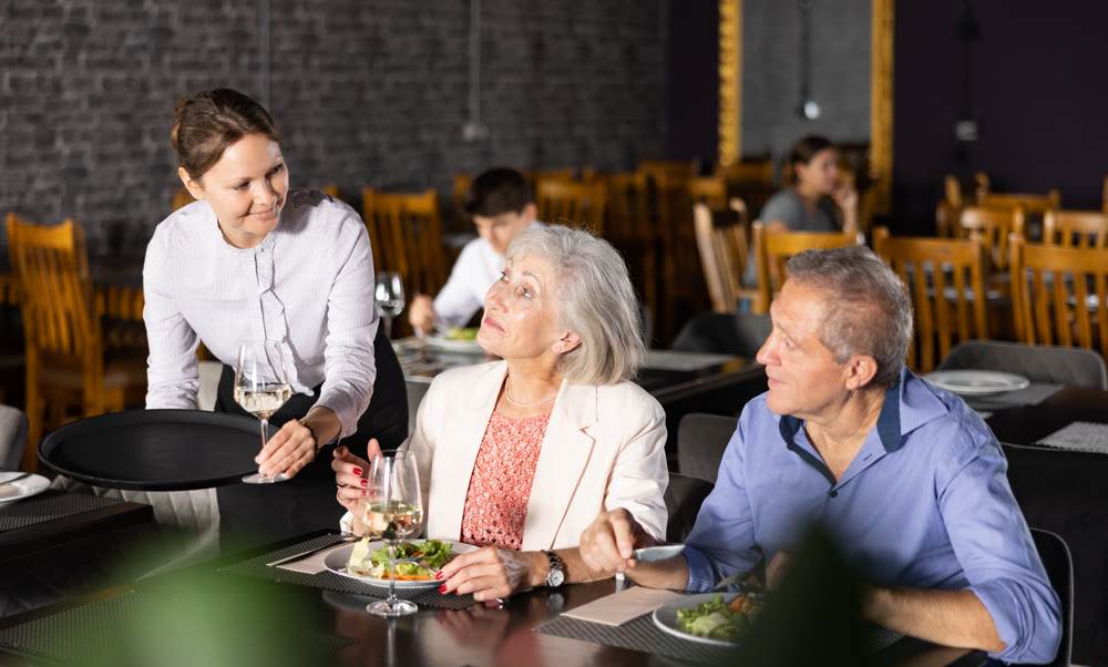 Female hostess serves puts on table order for elderly spouses