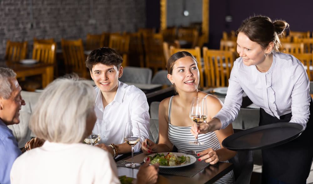 Female waiter serving wine to elderly couple and young couple in restaurant