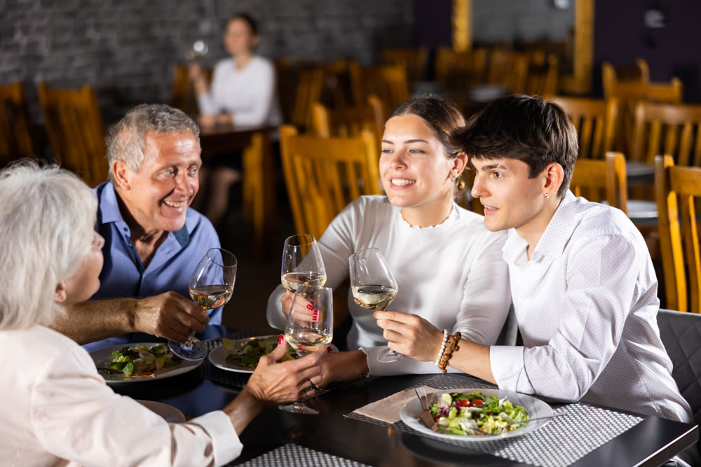 Young family and elderly couple of spouses eating in cafe celebrating event and communicating