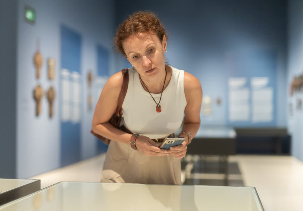 Attentive woman standing near exposition and looking with interest at art objects under glass in museum
