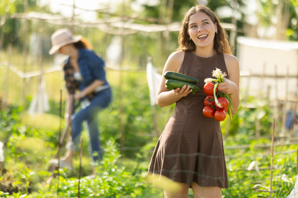 Positive woman in dress posing with tomatoes, zucchini and green onions in garden