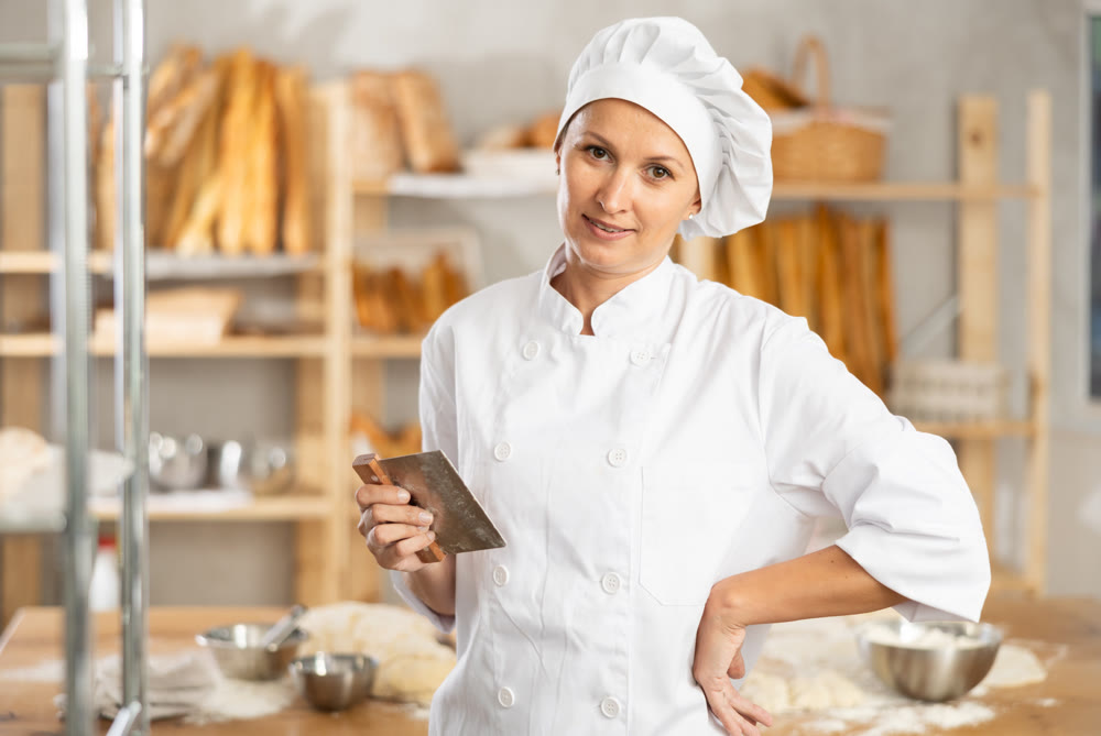 Woman baker cook stands against background of workspace with cutter
