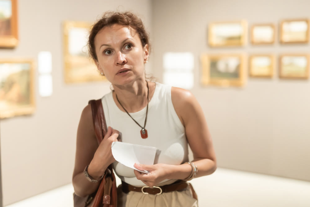 Young female visitor looking at exhibition in museum of ancient art