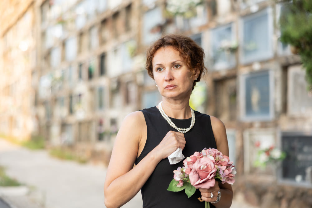 Drieving woman in black dress standing with bouquet by columbarium