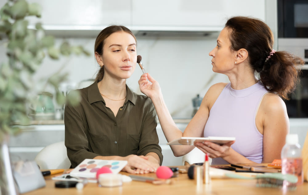 Female makeup artist brushing blush onto woman face