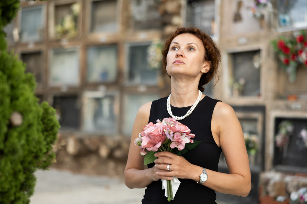 Woman in black mourning dress standing with flowers near columbarium