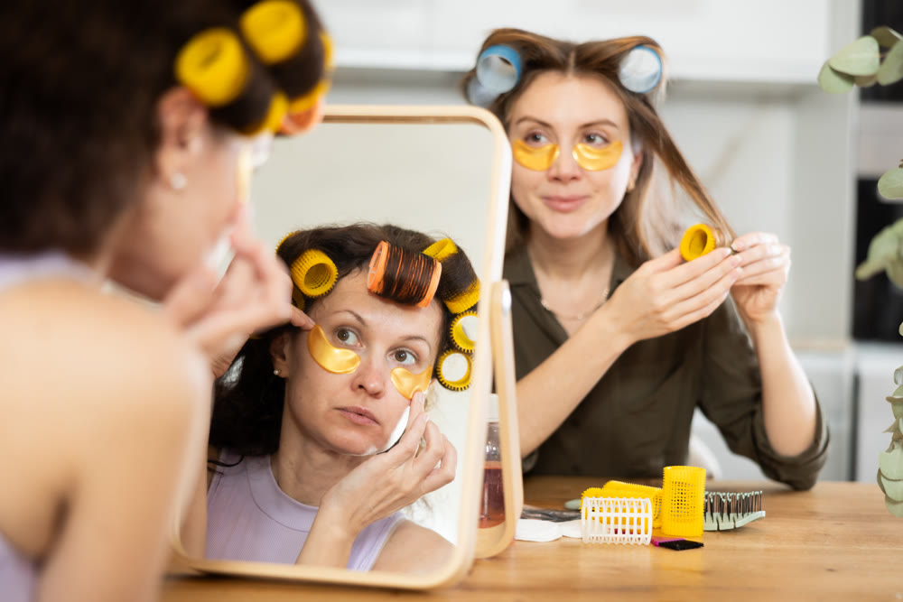 Women in colorful curlers applying eye patches and sharing beauty secrets