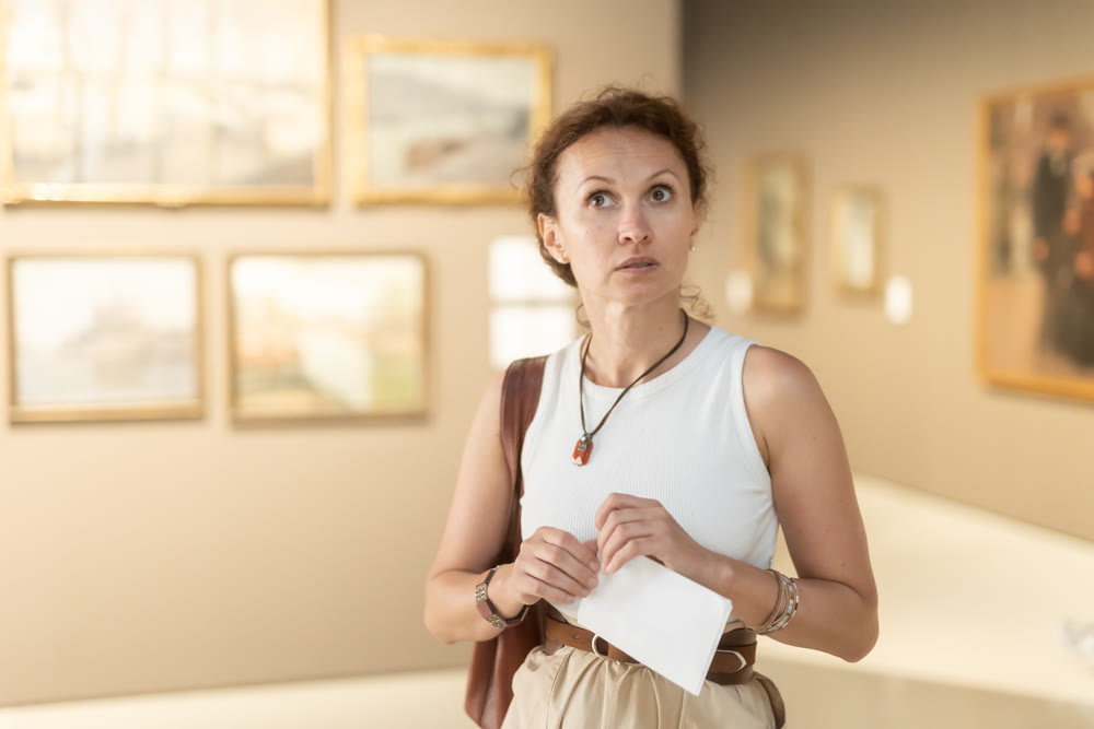 Young female visitor looking at exhibition in museum of ancient art