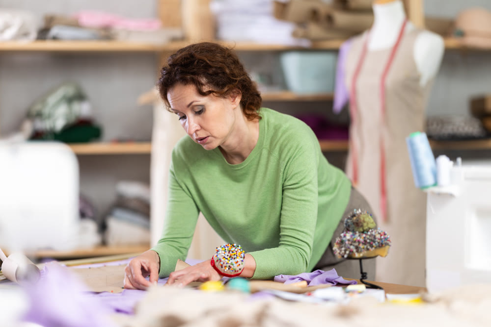 Female tailor pinning paper pattern to fabric in workshop
