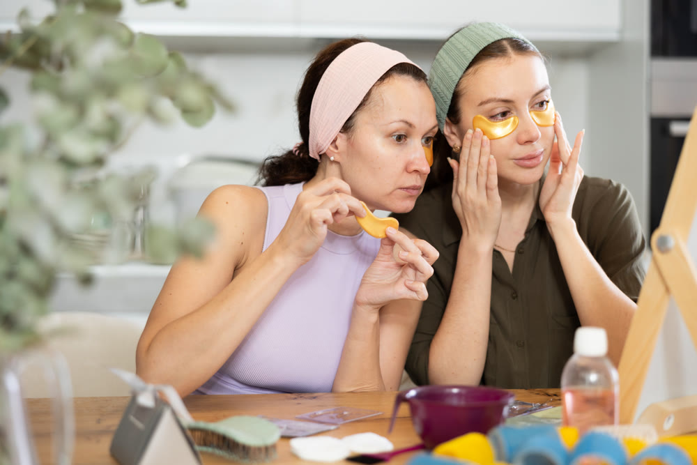 Two besties applying golden under-eye patches in home setting