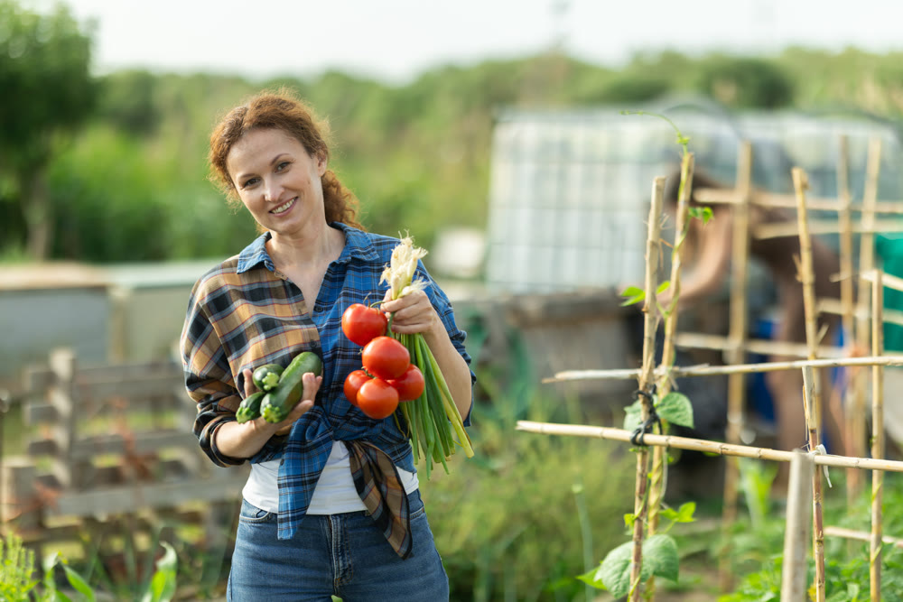 Woman shows off her harvest of zucchini, red tomatoes and green onions