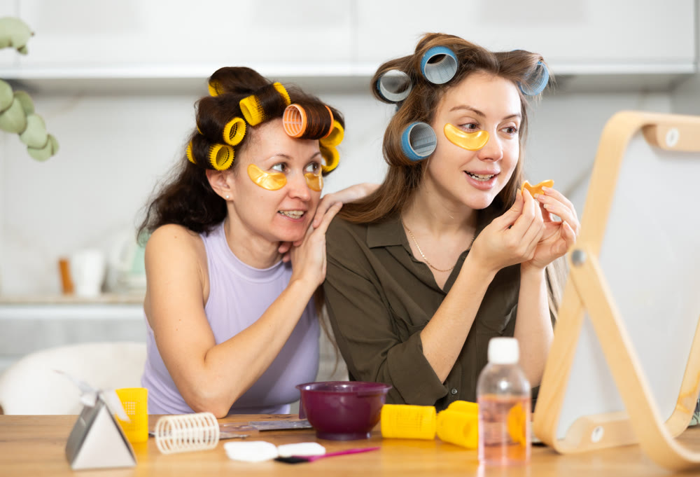Two women curl their hair with curlers and use patches
