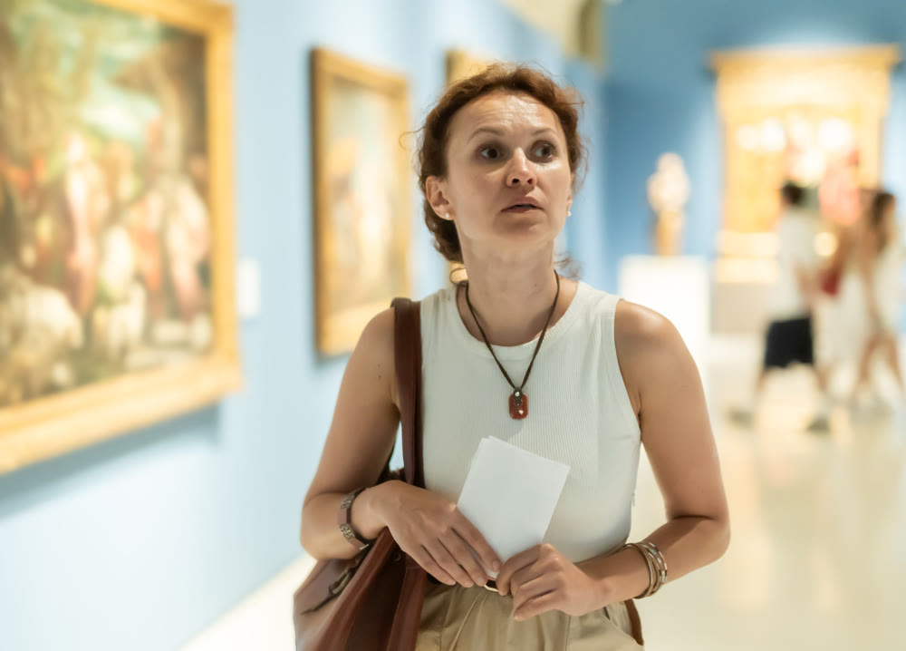 Attractive woman holding guide book in museum of arts and admiring works of art