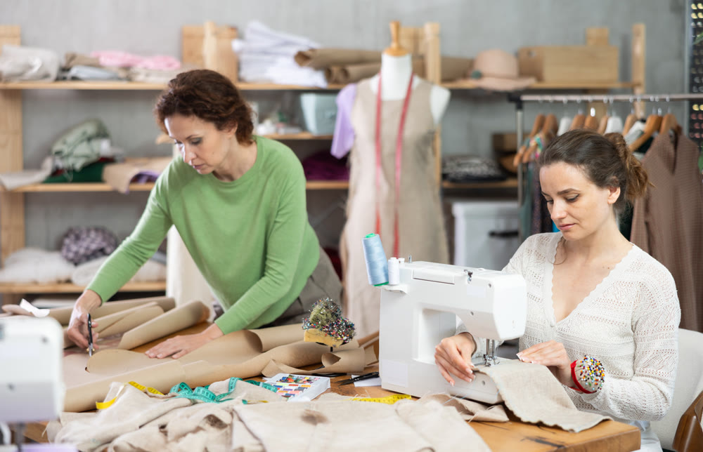 Woman tailor at work in cloth design shop. Apprentice cut out paper dress pattern