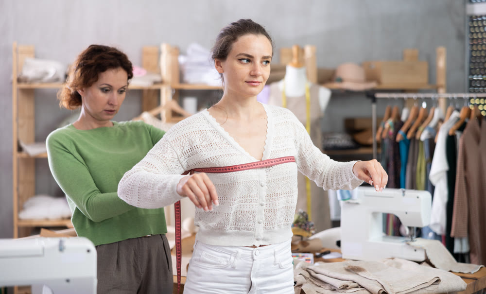 Woman tailor using measuring tape to measure clothes on girl in sewing workshop