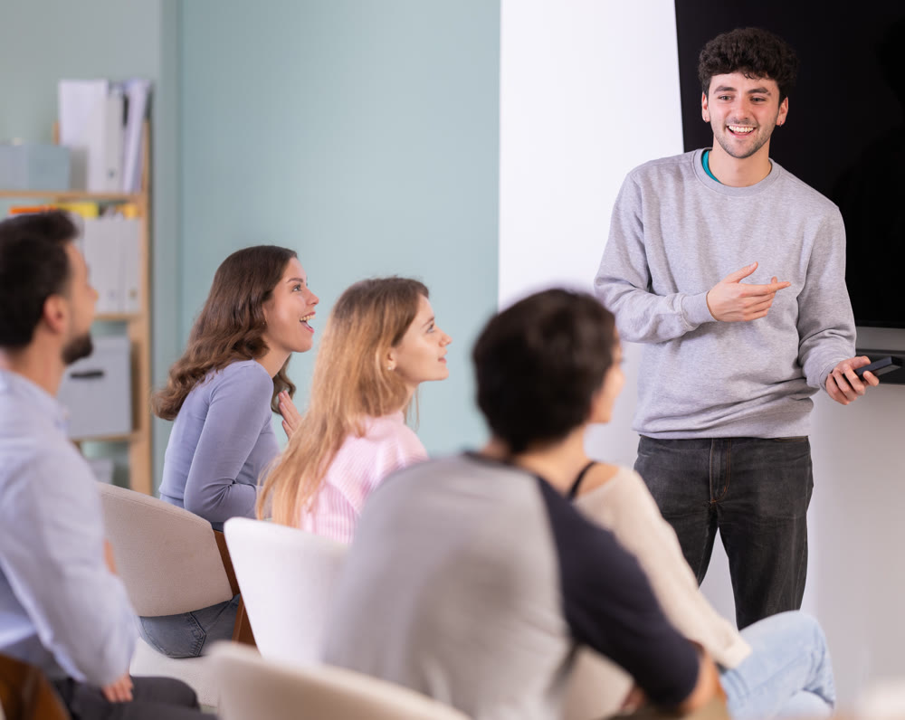 Male lecturer communicates with students, controls projector using remote control.
