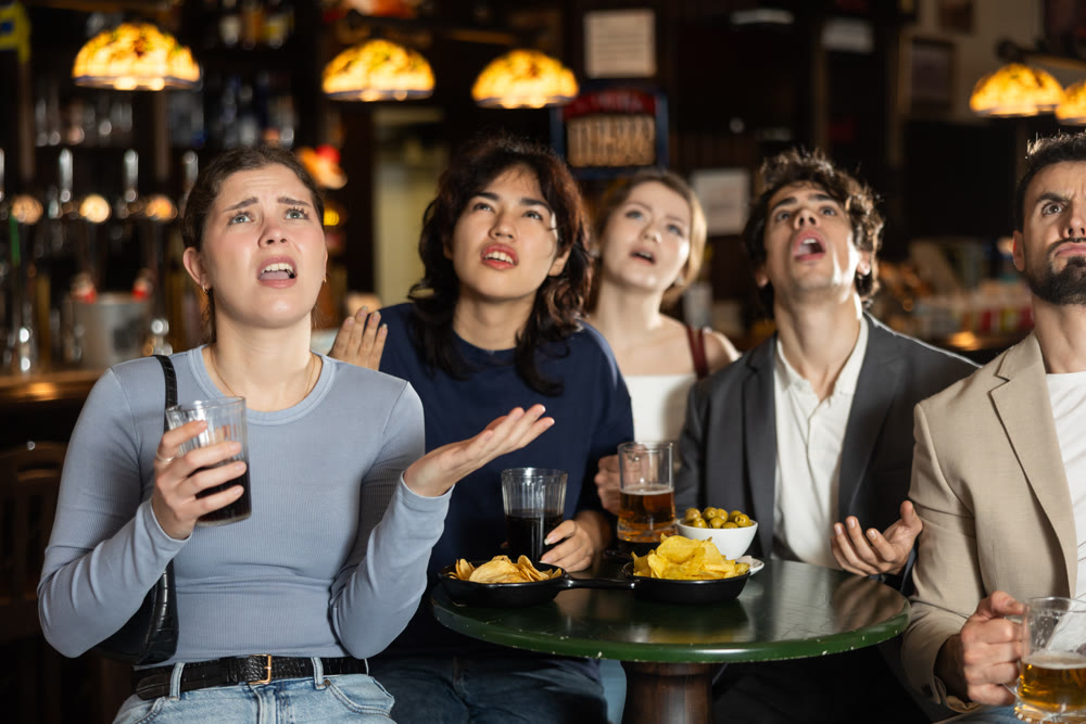 Group of young sports fans upset and worrying during game match on TV in beer pub