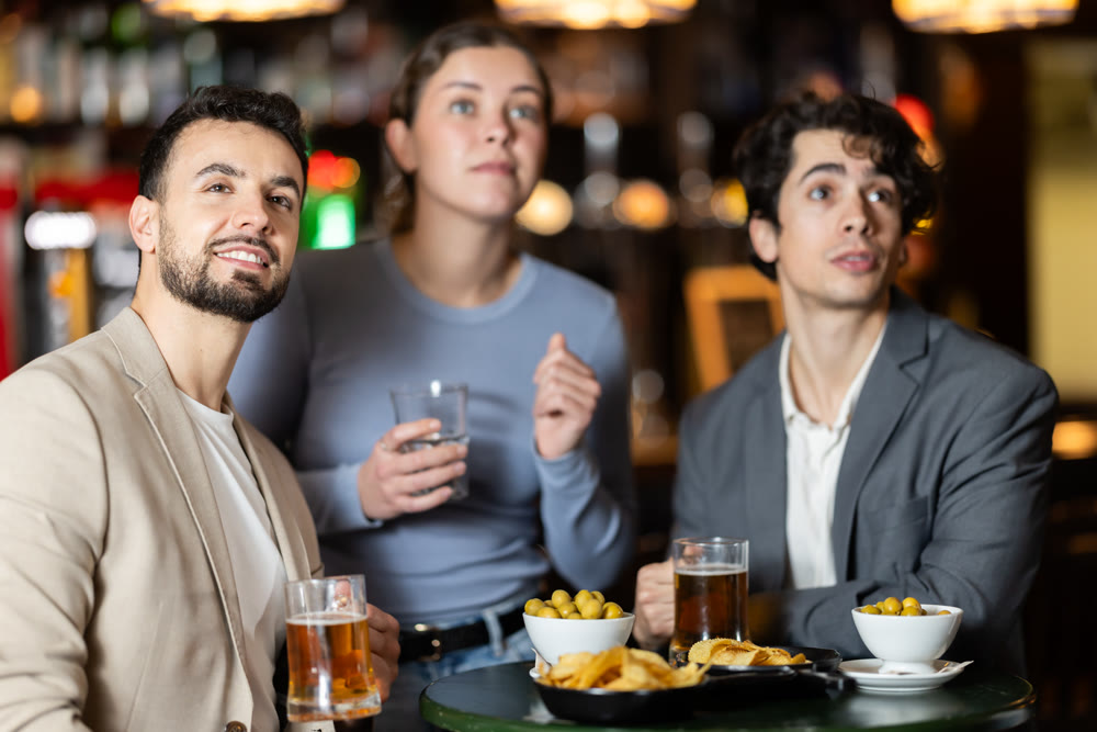 Group of excited young friends fans cheering for sports team together, watching match on TV in beer bar
