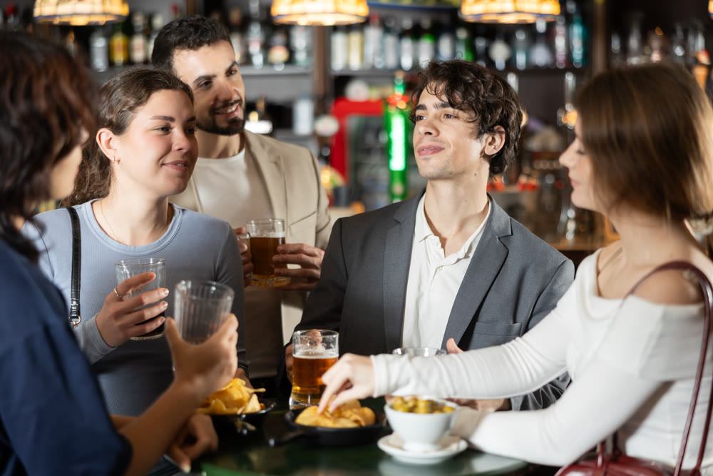 Young friends meeting at table in bar, discussion and drinking beer