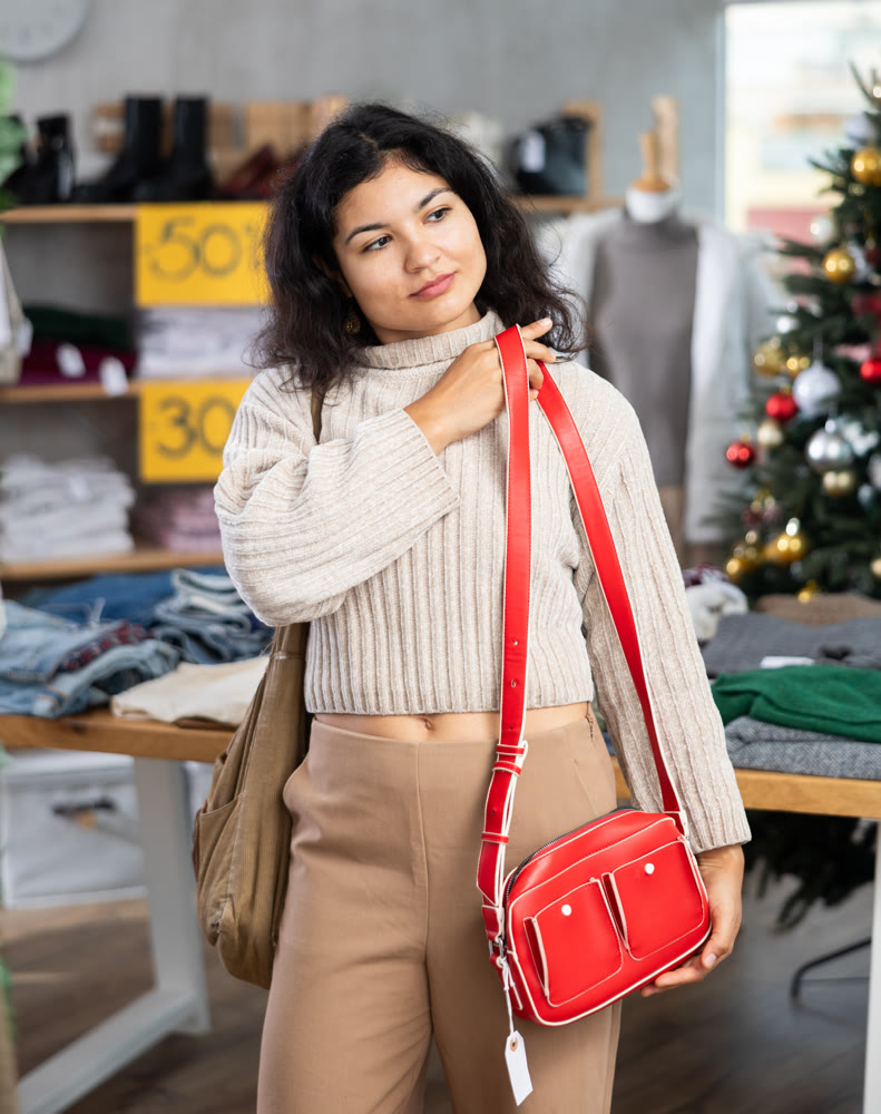 Latina woman happily chooses fashionable handbag in clothing store.